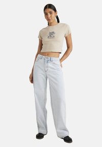 Beige cropped t-shirt with navy floral graphic and text paired with light blue wide-leg jeans. Black shoes complete the outfit.