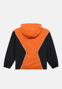 Ανάγλυφο αδιάβροχο μπουφάν με μπλοκ χρωμάτων που διαθέτει πορτοκαλί πάνω μέρος, μαύρες πλευρές και λευκή διακοσμητική ραφή. Με κουκούλα και ελαστικούς μανδύες.
