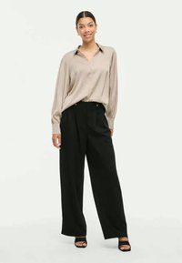 Bézs hosszú ujjú blúz gallérral, magas derekú fekete, bő szárú nadrággal párosítva. Sima anyag és laza szabás. Fekete magassarkú szandál.