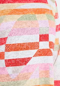 Lyhythihainen paita, jossa on monivärinen raidoitus punaisen, oranssin, vaaleanpunaisen ja vihreän sävyissä, koristeena pinnalla kimaltelevia kivisiruja.