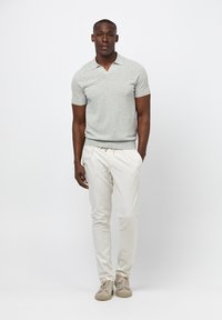 Ljusgrå kortärmad polotröja med ribbad nederkant, ihop med vita slim fit byxor och beige sneakers, står på en enfärgad bakgrund.