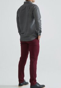 Chemise à boutons grise à motifs, pantalon bordeaux et chaussures noires à semelle légère. Présente un col standard et des manches longues.