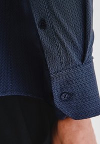 Granatowa koszula zapinana na guziki z teksturowanym wzorem. Posiada mankiet z ciemnym guzikiem i dopasowany krój.