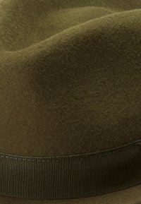 Close-up of a green felt hat featuring a dark band, highlighting its smooth texture and elegant design.