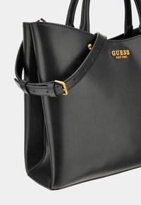 Sac à main en simili cuir noir avec une forme structurée, équipé de matériel en or, d'une bandoulière amovible et du logo de la marque en relief à l'avant.