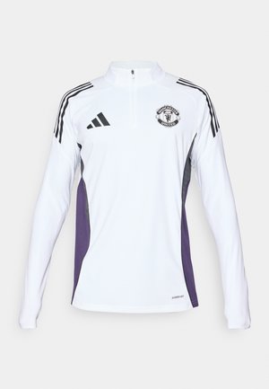 Chemise d'entraînement blanche à manches longues avec fermeture éclair mi-hauteur, rayures noires, panneaux latéraux violets et logo de Manchester United sur la poitrine.
