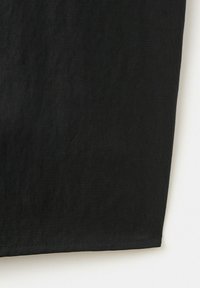 Gros plan sur un tissu noir avec une texture de tissage diagonal visible et un ourlet droit cousu sur fond blanc.