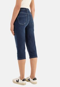 Tummansiniset farkkukaprihousut, joissa on keskikorkea vyötärö, kaarevat takataskut ja kantattu helma, yhdistettynä valkoisiin tennareihin.