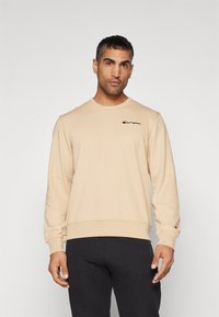 Beiger Sweatshirt mit langen Ärmeln, Rundhalsausschnitt und gesticktem "Champion"-Logo in Schwarz auf der linken Brust. Hergestellt aus weichem Stoff.
