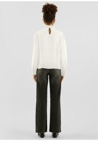 Witte blouse met lange mouwen, een geplooide hoge kraag, een keyhole-detail aan de achterkant en gestructureerde mouwen, gecombineerd met donkere jeans met wijde pijpen.