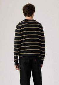 Svart randig sweatshirt med gula horisontella linjer, ribbade ärmslut och nederkant, avslappnad passform, mjukt material, synliga sömnadsdetaljer.