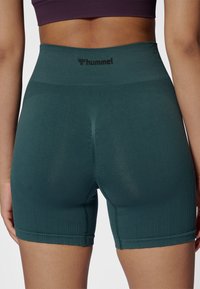 Groene, hoog getailleerde, aansluitende short van rekbare stof met een geribbelde textuur en een zwart logo op de tailleband.