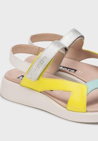 Sandalias multicolores con una correa metálica plateada, acentos de cuero amarillo y aqua, y una suela gruesa blanca.