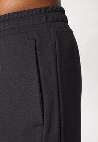 Calças atléticas pretas feitas de um tecido suave e texturizado, com um cós elástico e bolsos laterais, apresentando um corte descontraído e um design plissado.