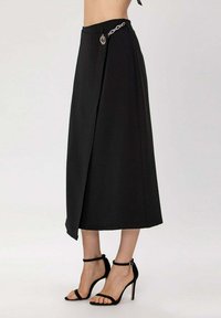 Jupe midi noire avec un design croisé, ornée d'une chaîne argentée à la taille. Fabriquée en tissu léger avec une texture douce.
