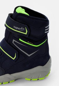 Navyblaue Knöchelstiefel mit grünen Akzenten, aus Textil und Wildleder gefertigt, mit Klettverschlüssen, Gummisohle und wasserdichtem Gore-Tex-Branding.