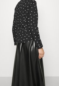 Czarna bluzka w kropki z długimi rękawami i zapięciem na guziki z przodu, połączona z czarną spódnicą z sztucznej skóry o wysokim stanem, o gładkiej teksturze.