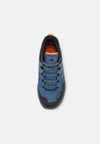 Niebieskie i czarne buty sportowe z siateczkową cholewką, pomarańczowymi akcentami i teksturowaną gumową podeszwą. Posiada sześć otworów na sznurowadła i sznurówki.