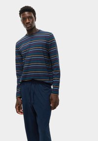 Camicia a maniche lunghe a righe blu navy con linee rosse, verdi e gialle; abbinata a pantaloni blu navy con cintura elasticizzata.