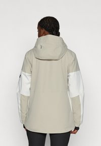 Beige veski veekindel jakk kapuutsiga, millel on valged varrukad ja tekstuurīga kangas. Tagaküljel on logo detail, mis pakub moodsat disaini.