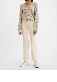 Pull tricot multicolore à manches longues et décolleté en V, associé à un jean droit beige pâle et des baskets montantes blanches.