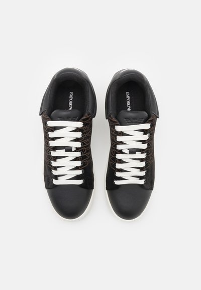 Scarpe da ginnastica nere con lacci bianchi, con una parte superiore a motivi, punta nera liscia e suola in gomma bianca a contrasto.
