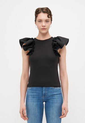 Black sleeveless top with ruffled fabric accents on shoulders; fitted silhouette; smooth texture; paired with blue denim jeans.