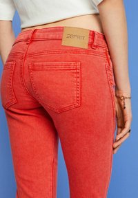 Jean en denim rouge avec une coupe ajustée, doté de poches arrière et d'une étiquette en cuir portant la mention "ESPRIT" sur la ceinture. Texture lisse.