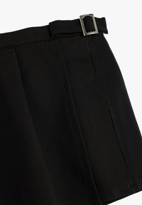 Pantalones cortos negros de tela suave, con una cinturilla ancha y un detalle de hebilla plateada. El diseño incluye pliegues marcados en la tela.