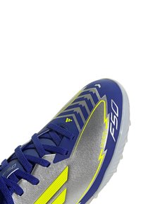 Blue and silver soccer shoe featuring a textured upper, neon yellow accents, and a streamlined design with black laces and patterned sides.