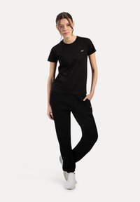Camiseta negra y pantalones jogger a juego, fabricados en un tejido suave. La camiseta presenta un pequeño logo, y los pantalones jogger tienen bolsillos y un corte ajustado.