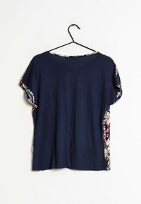 T-shirt blu navy con maniche corte a fantasia floreale. Tessuto morbido, vestibilità ampia, scollo rotondo, appeso a una gruccia nera.