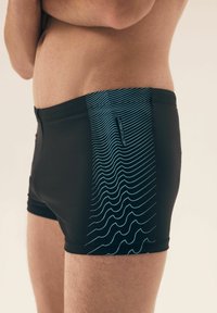 Czarne kąpielówki wykonane z gładkiego materiału, z niebieskim wzorem fal wzdłuż boku i dopasowanym krojem.