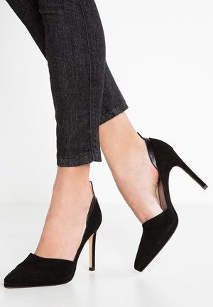 Czarne zamszowe szpilki z wydłużonym noskiem i odkrytą piętą, z wąskim obcasem typu stiletto.