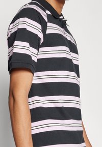 Randig polo i mörk marinblå med ljusrosa och vita horisontella ränder. Har en klassisk krage och korta ärmar. Mjukt tyg.