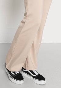 Beige, aansluitende sweatpants met een gladde textuur, gecombineerd met zwart-witte lage sneakers met een klassiek ontwerp en contrasterende details.