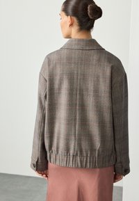 Giacca a quadri marrone con vestibilità rilassata, con collo, bottoni sulle maniche e orlo elasticizzato. Indossata sopra una gonna rosa.