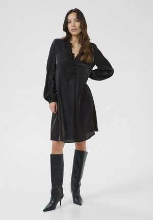 Black dress with a V-neckline, textured fabric, and floral embellishments. Paired with high, pointed black boots, creating a sleek silhouette.