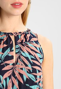 Top senza maniche floreale realizzato in tessuto leggero, con uno sfondo blu navy e motivi di foglie rosa e turchesi, e un dettaglio con scollatura a chiave.