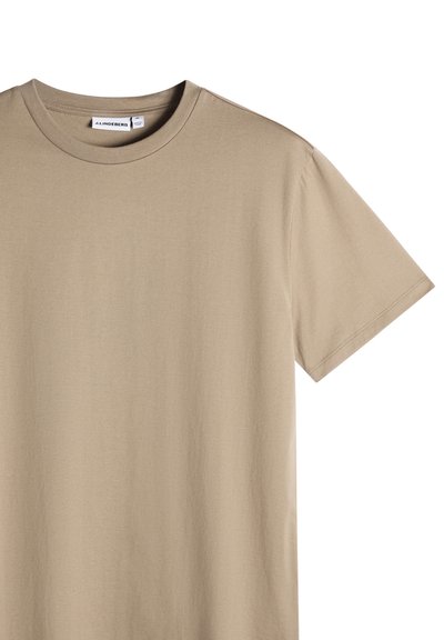 Maglietta beige a maniche corte con scollo rotondo e etichetta del marchio J.Lindeberg visibile all'interno del colletto.