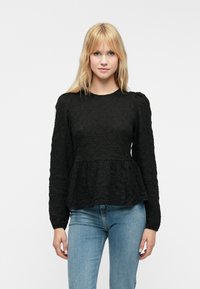 Czarna, strukturalna bluzka z długim rękawem, zaprojektowana w stylu peplum, z okrągłym dekoltem i lekko puffowanymi rękawami. Połączona z jasnoniebieskimi dżinsami.