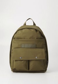 Olivengrønn ryggsekk med avrundet form, laget av slitesterkt stoff. Har en frontlomme med klaff og trykknapp-lukking. Justerbare skulderstropper.