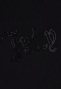 Juodos medžiagos audinys su blizgančiu "Juicy" užrašu, papuoštu juodais ir sidabriniais kristalais, esantis ant lygios tekstūros.