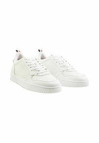 Weiße Sneaker mit einem glatten synthetischen Obermaterial, durchbrochenen Details, flachen Schnürsenkeln und einer strukturierten Gummisohle. Akzentuiert mit roten und blauen Streifen.