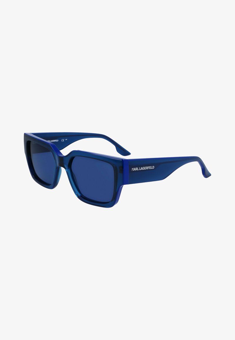 Niebieskie okulary przeciwsłoneczne z masywną plastikową oprawą, kwadratowymi soczewkami i delikatnym Gradientem. Nazwa marki "KARL LAGERFELD" na zauszniku.