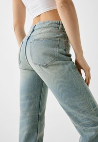 Blå denimjeans med hög midja, ljus tvätt och strukturerad passform. Har två bakfickor och subtila slitningar på tyget.