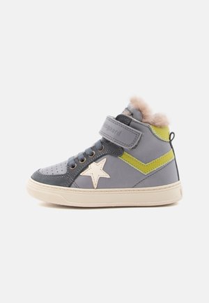 Szary sneaker na wysokiej cholewce z beżową gumową podeszwą, białym detalem w kształcie gwiazdy, zielonym paskiem, rzepem, sznurowadłami i jasnobrązową futrzaną podszewką wewnątrz.