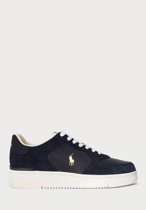 Navy suede sneaker with smooth leather accents, white rubber sole, and contrasting gold logo on side. Features white laces and round toe design.