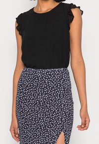 Haut noir sans manches avec des emmanchures volantées, associé à une jupe ajustée bleu marine avec des motifs floraux blancs et une fente latérale.