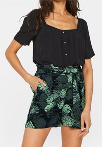 Svart blus med korta ärmar och fyrkantig halsringning, kombinerad med mönstrade gröna shorts med bladmotiv, med knytmidja och sidofickor.